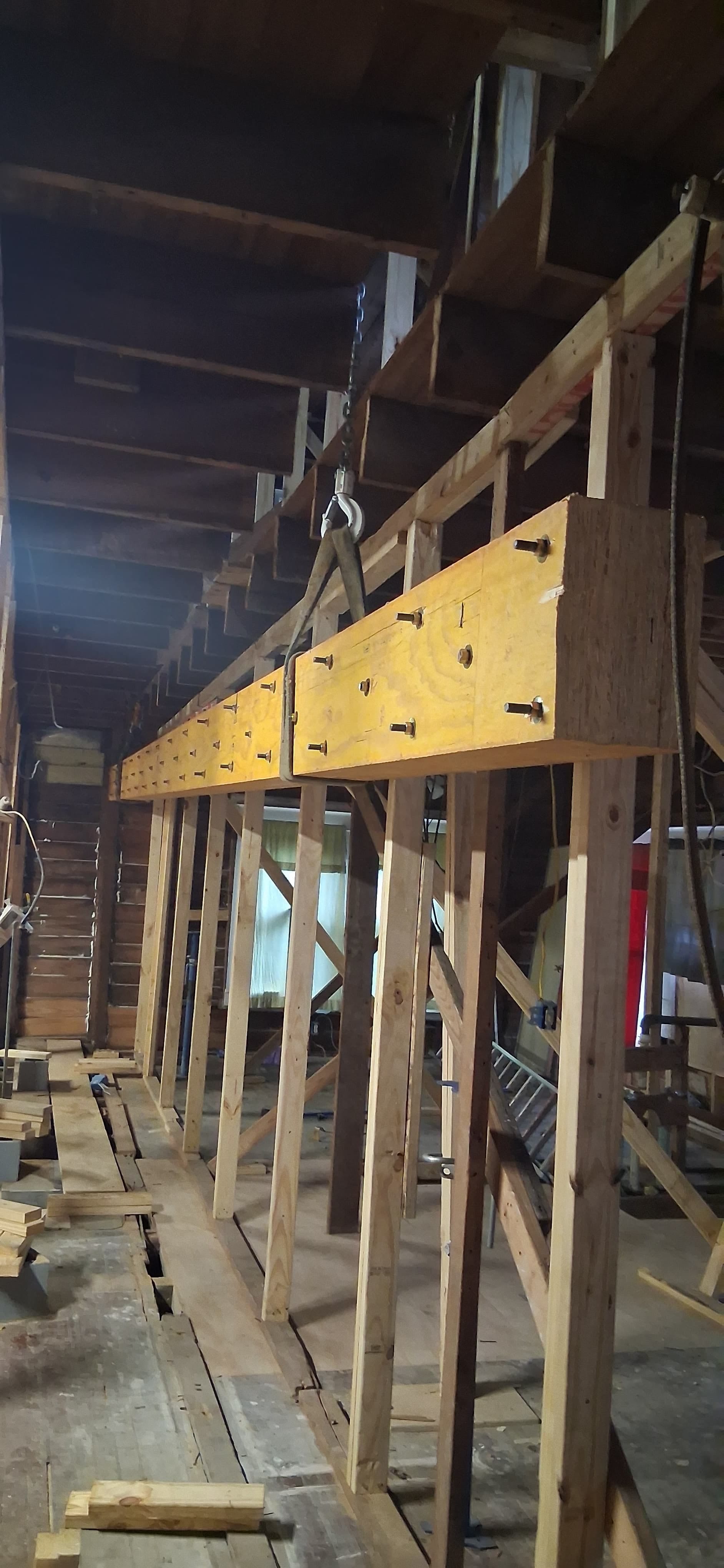 Bolted wood beam suspended by lifting straps inside exposed interior framing with temporary wood supports.
