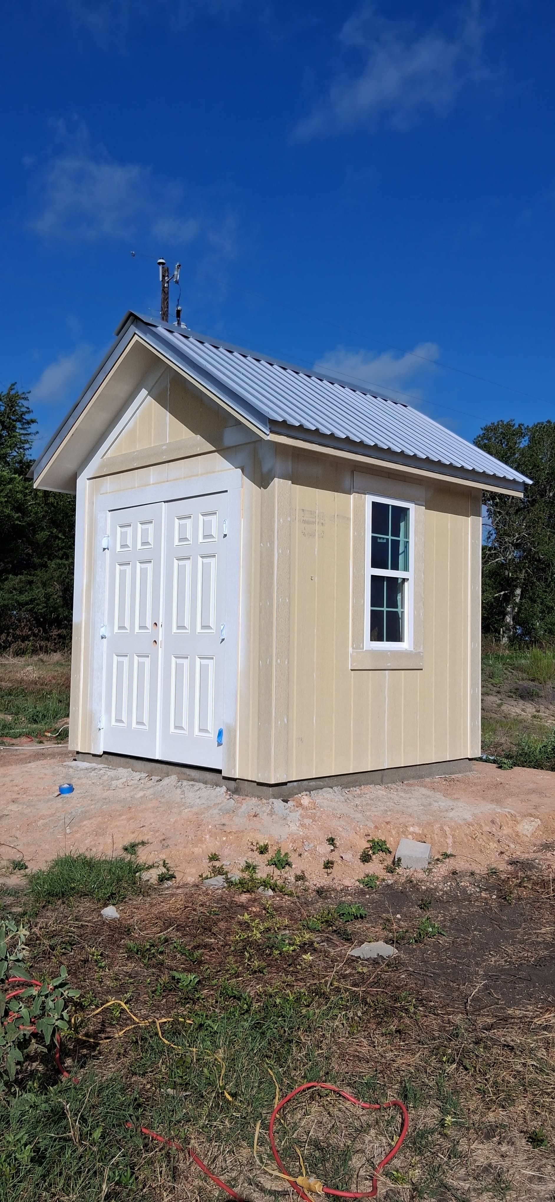 Small exterior structure with yellow siding and white double doors before exterior painting.