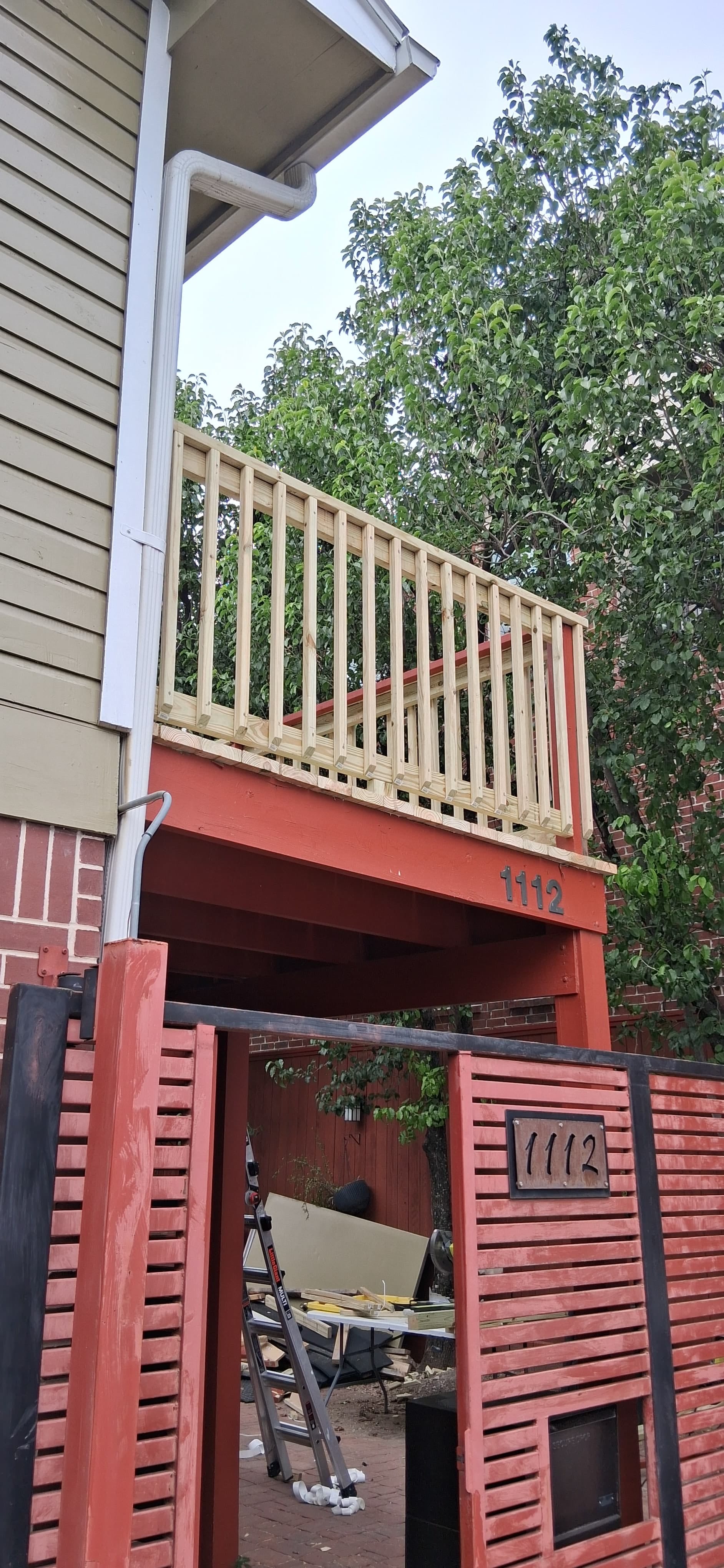 New unpainted wood railing and balusters installed on the same elevated deck above the existing red-painted structure.