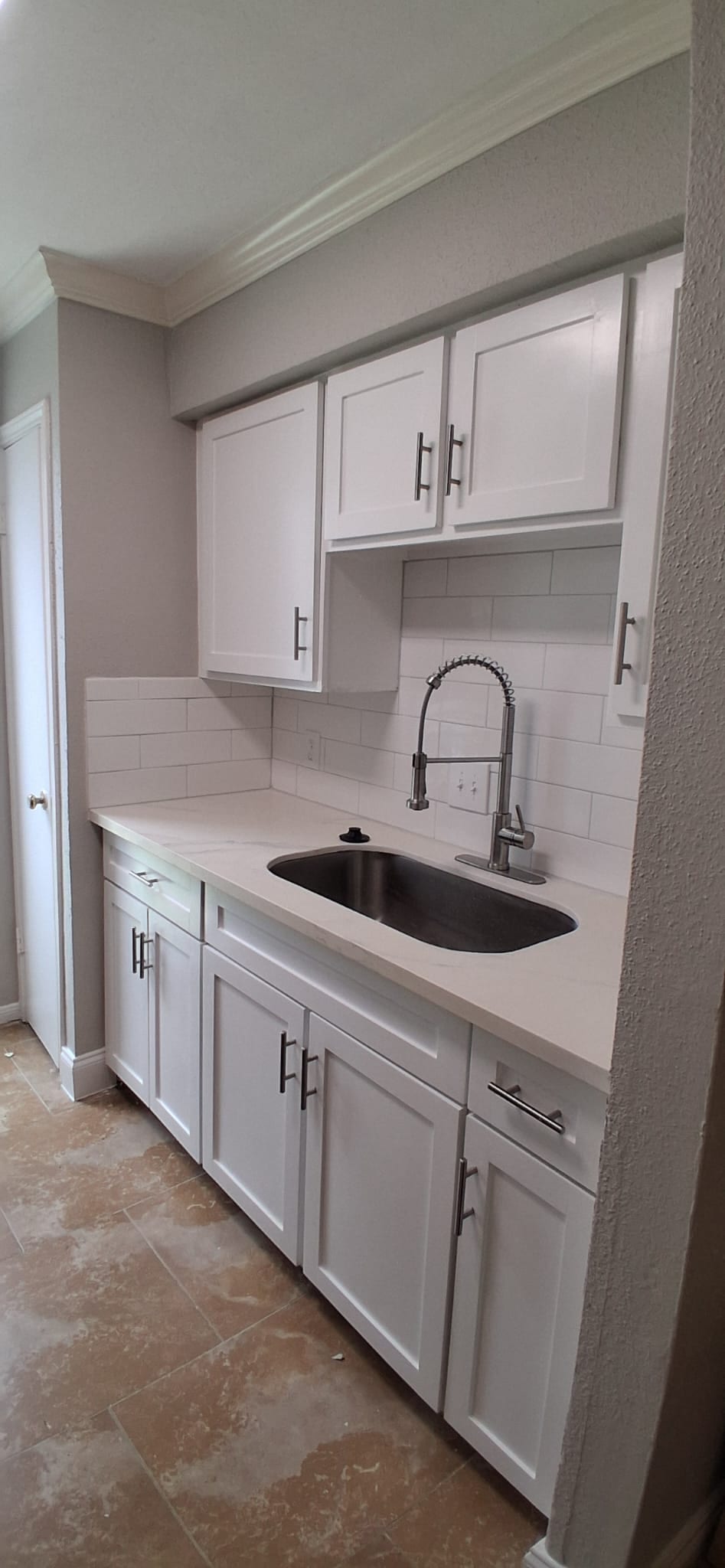 Sink area of the same kitchen after installation of painted white cabinets, hardware, a countertop, tile backsplash, sink, and faucet.