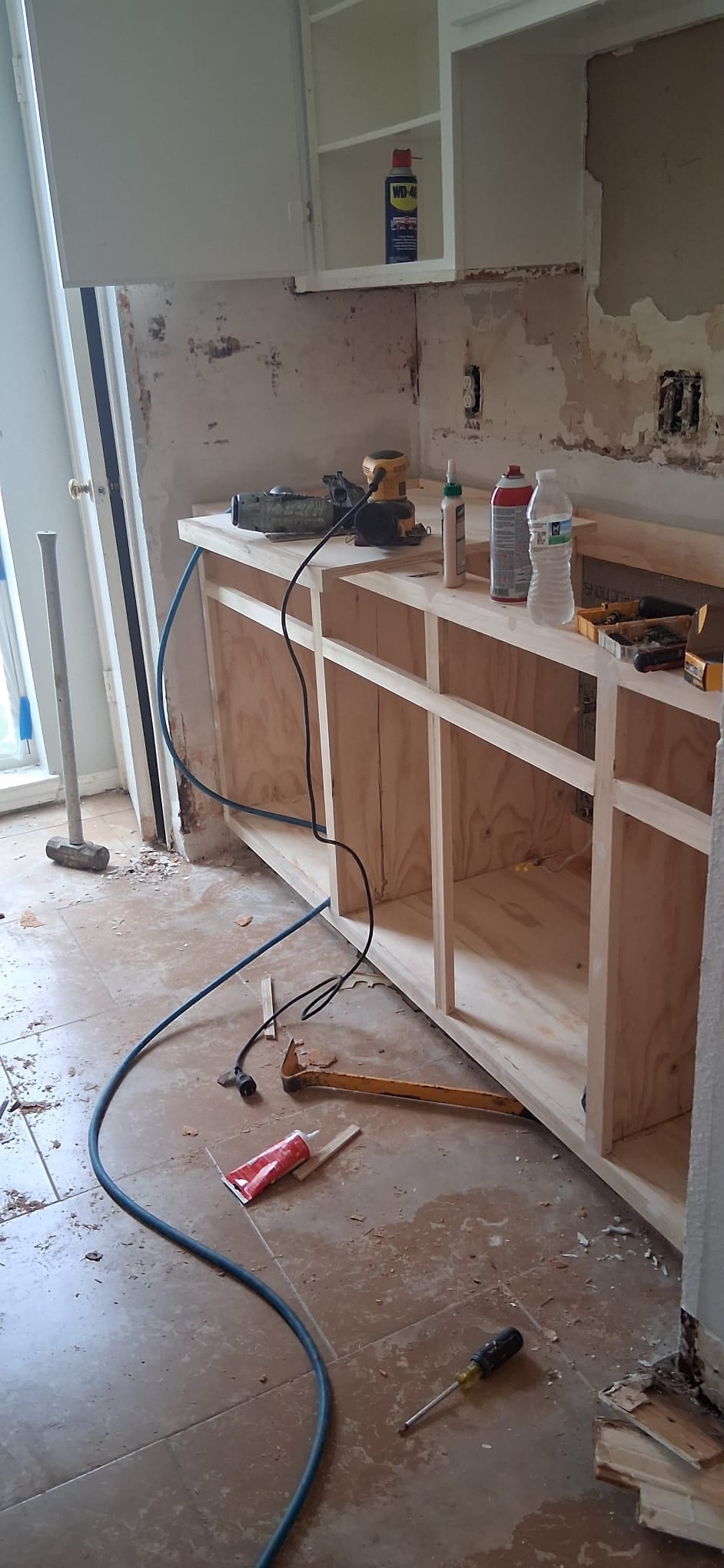 Sink-side kitchen cabinet boxes with tools and unfinished wall surfaces before cabinet doors, countertop, and sink are installed.