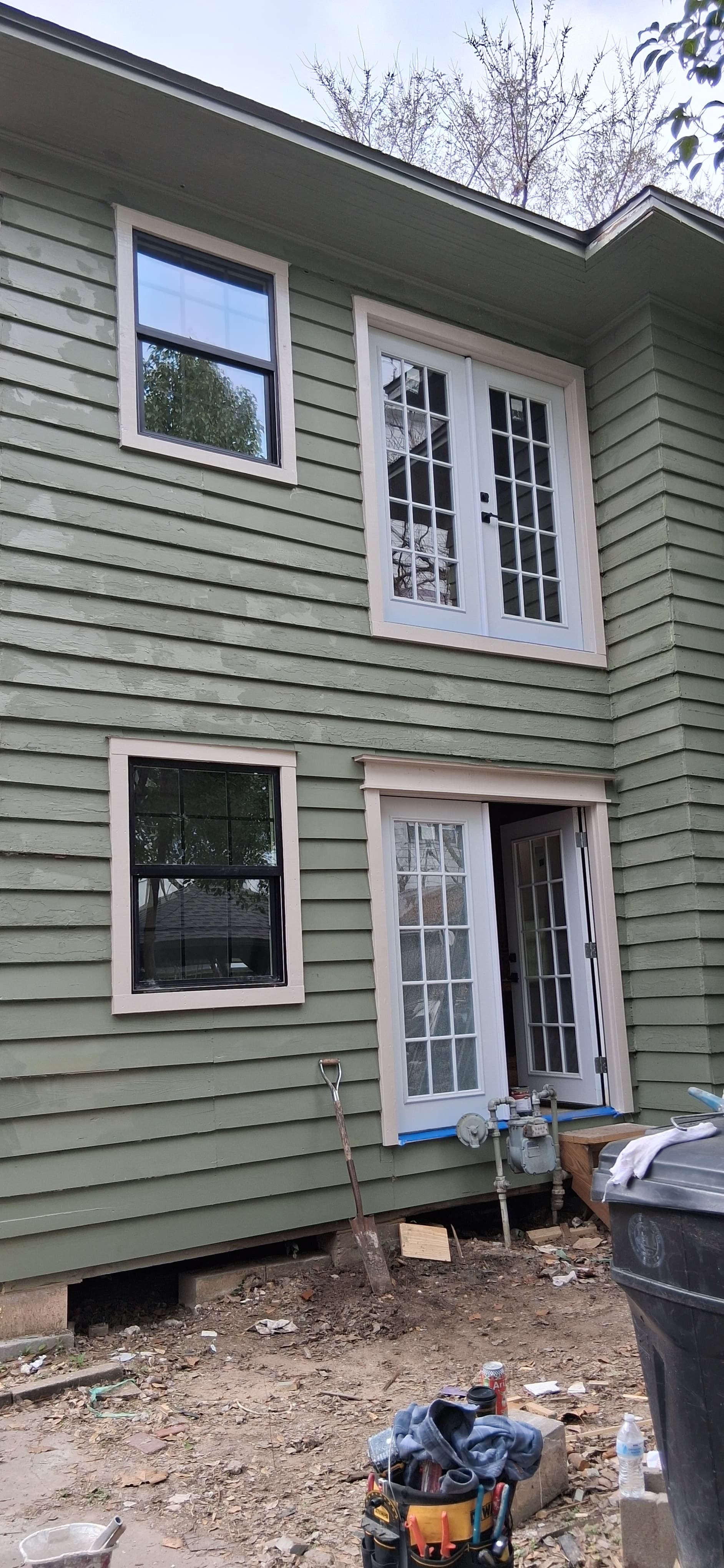 Rear of the same house after window and exterior trim installation, with siding repairs around the window and door openings before final painting.