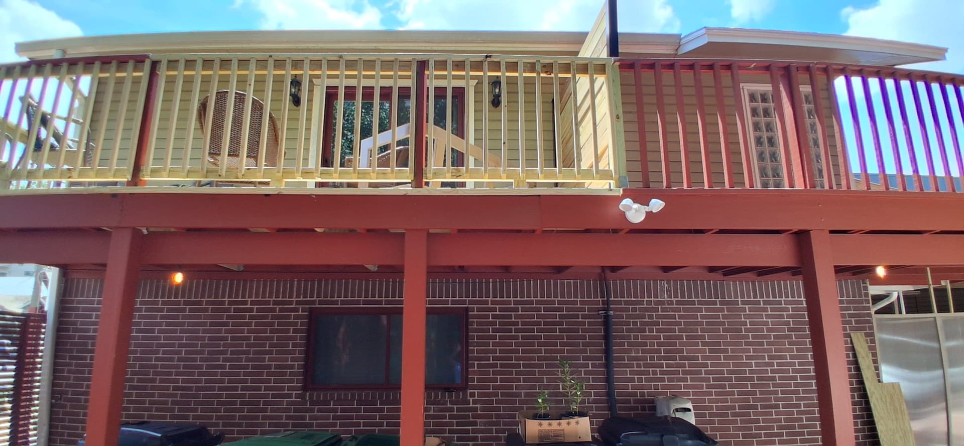 Wide exterior view of the same second-story deck with new unpainted wood railing above the existing red-painted structure.