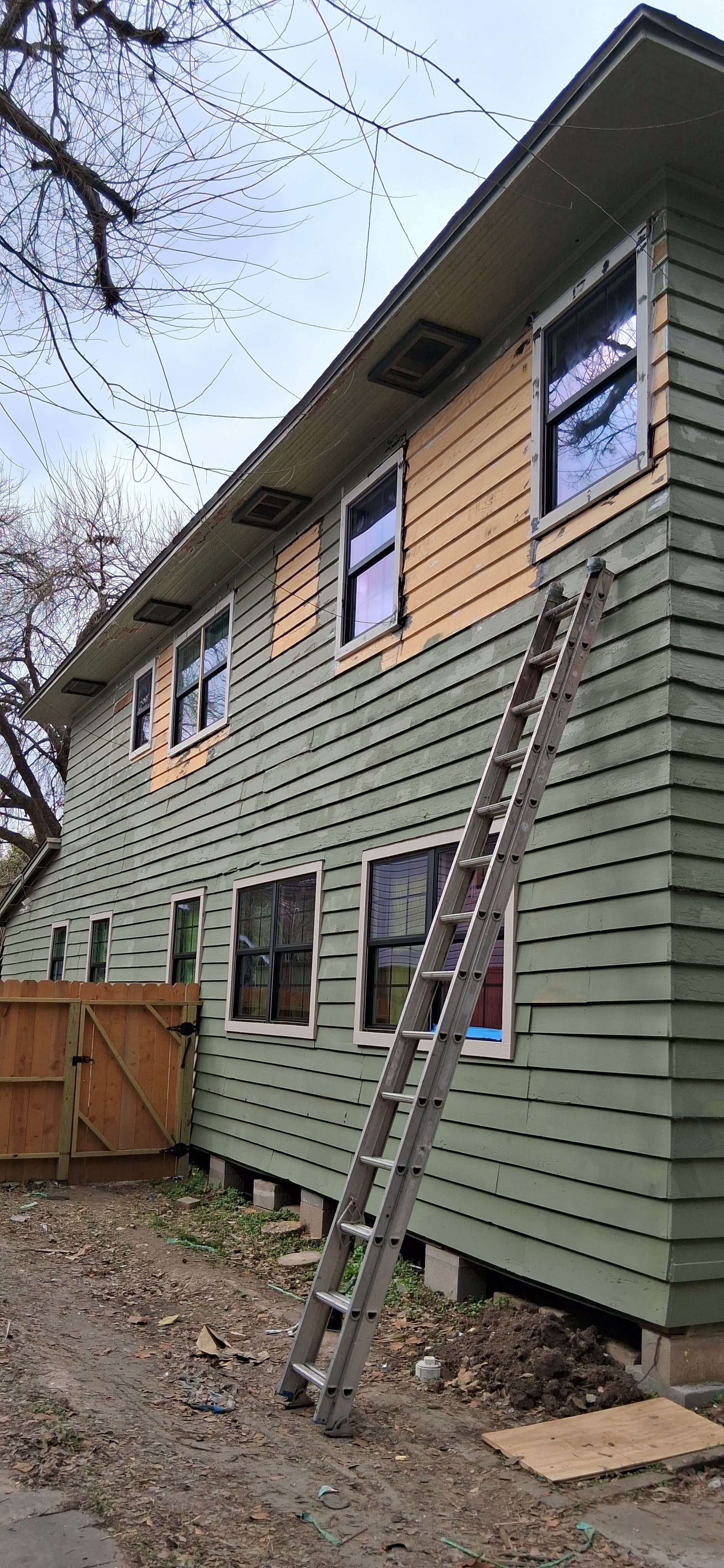 Side of the same house after window installation, showing new windows, exterior trim, and unpainted siding repairs around upper openings.