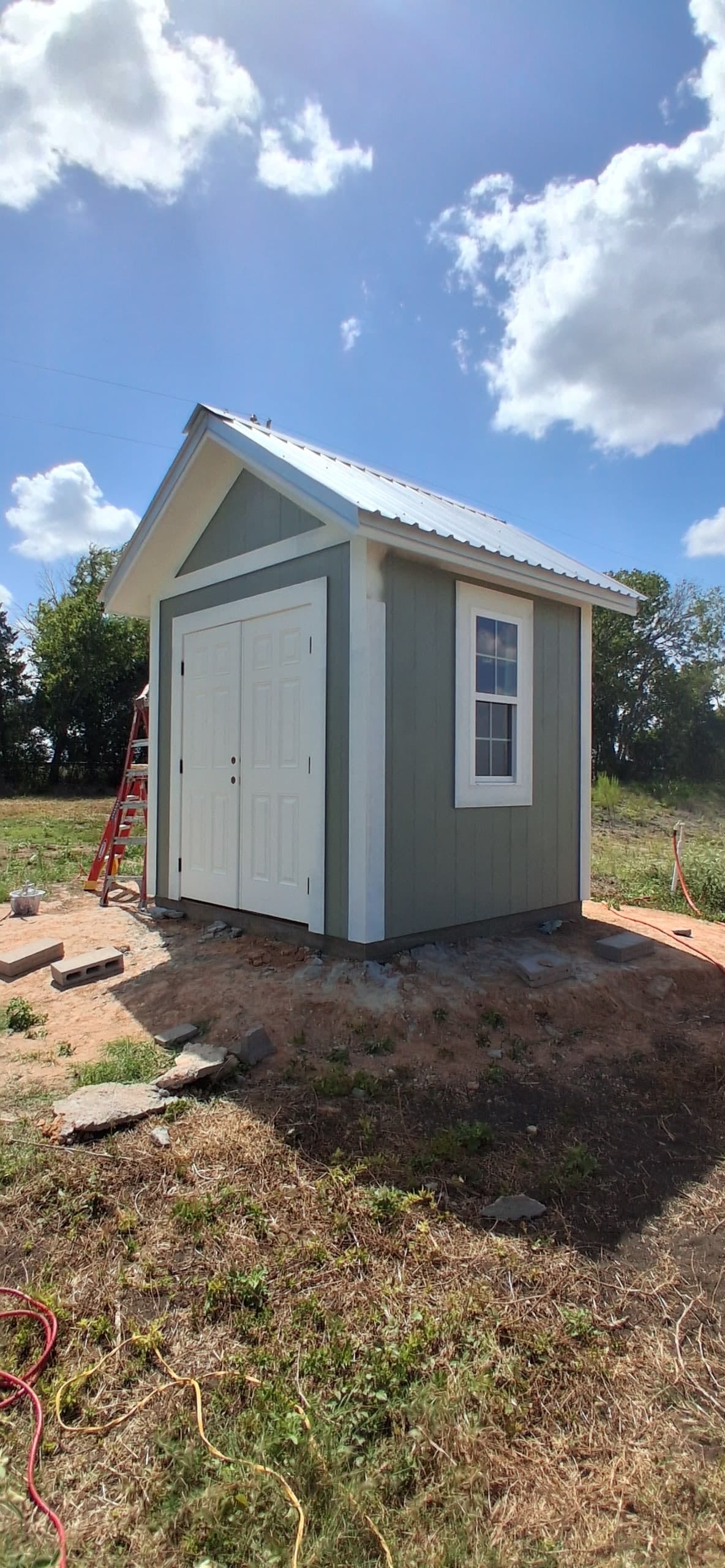 The same small exterior structure after painting, with green siding, white trim, and white double doors.