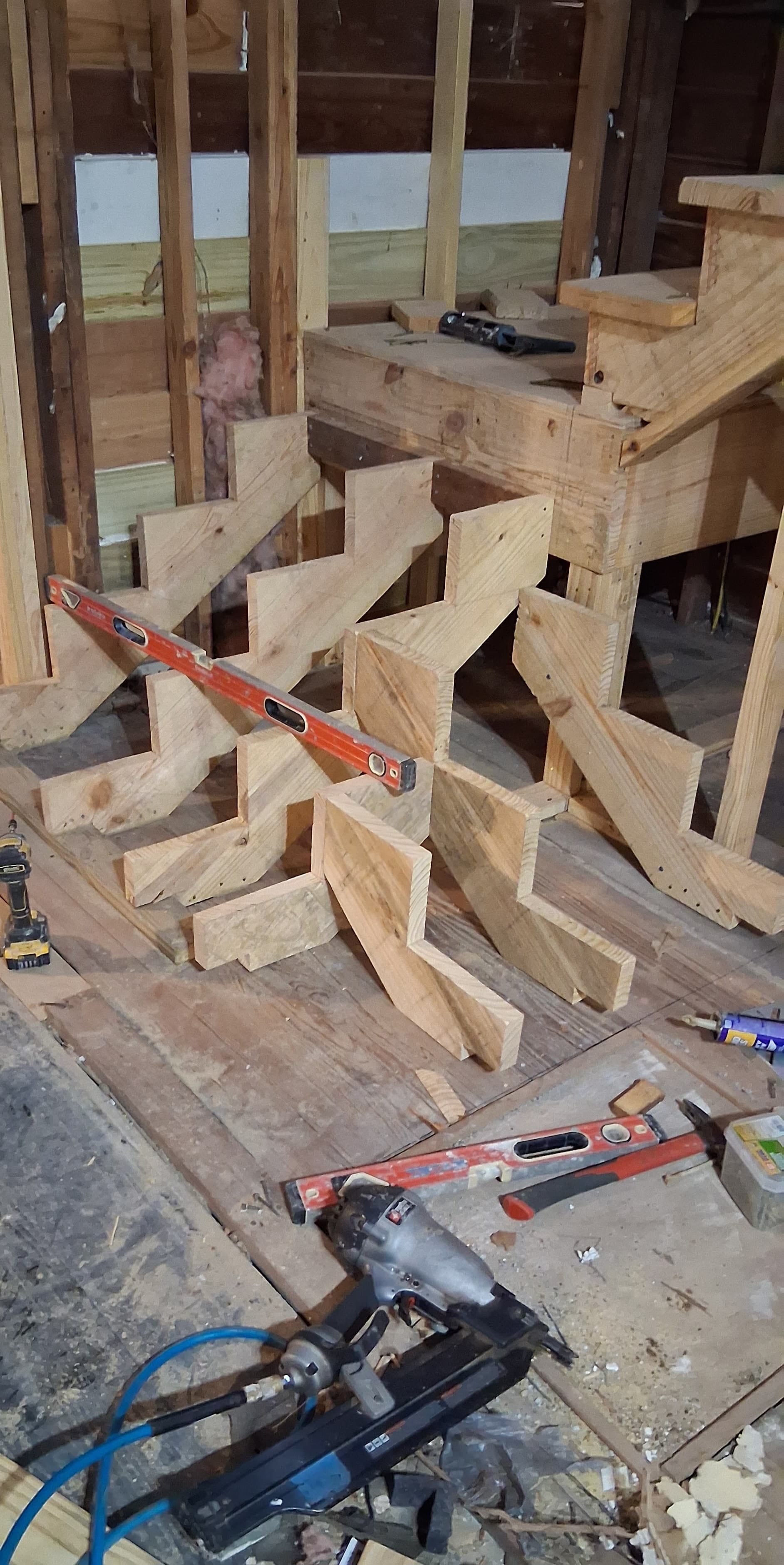 Cut wood stair stringers being positioned beside a framed landing before the treads are installed.