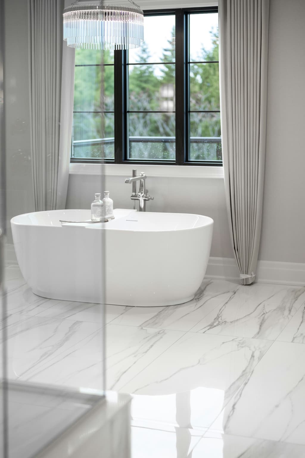 Freestanding tub with polished marble floor, chandelier, and soft drapery.