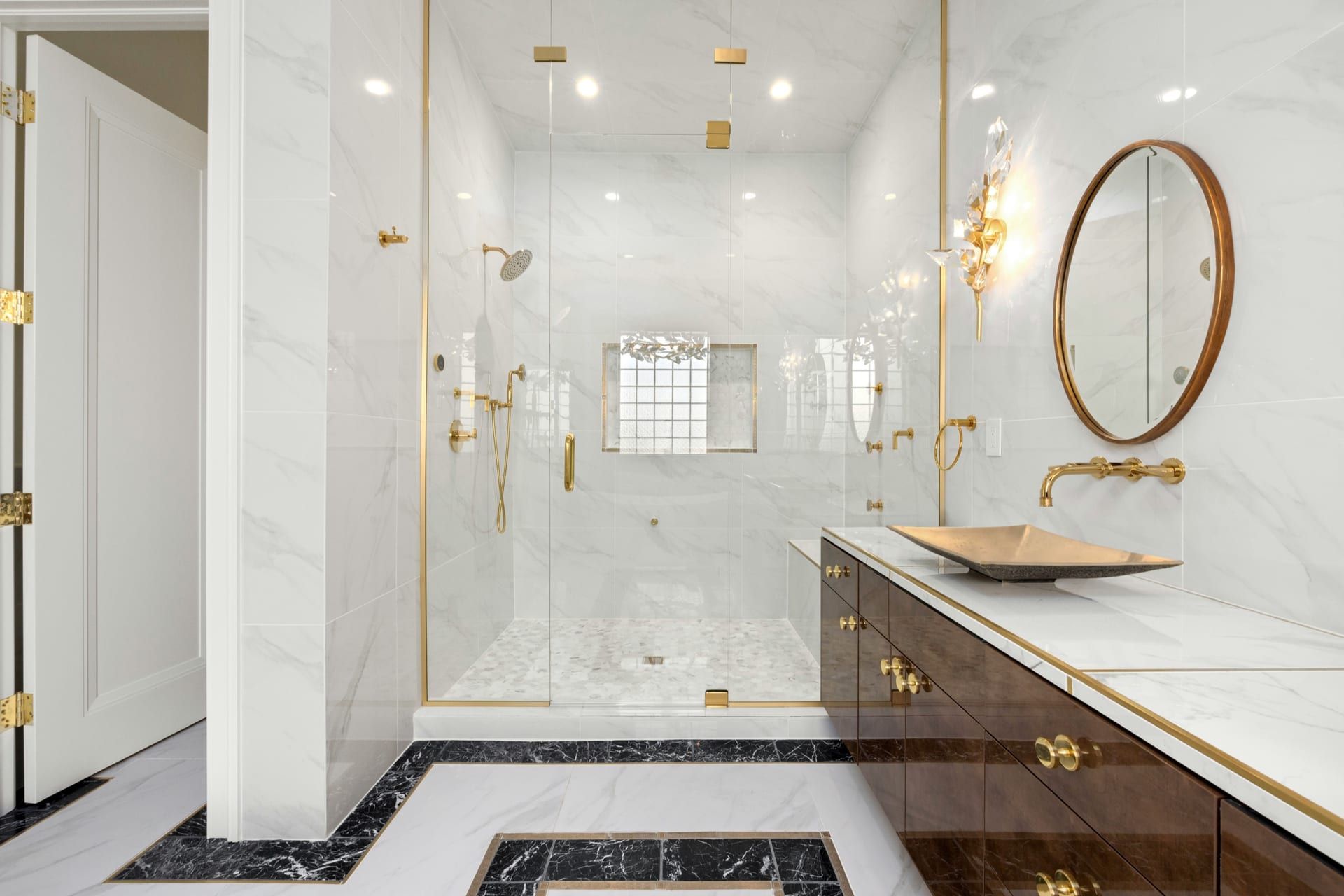 Luxury primary bathroom with marble-look tile, brass hardware, glass shower, and freestanding tub.