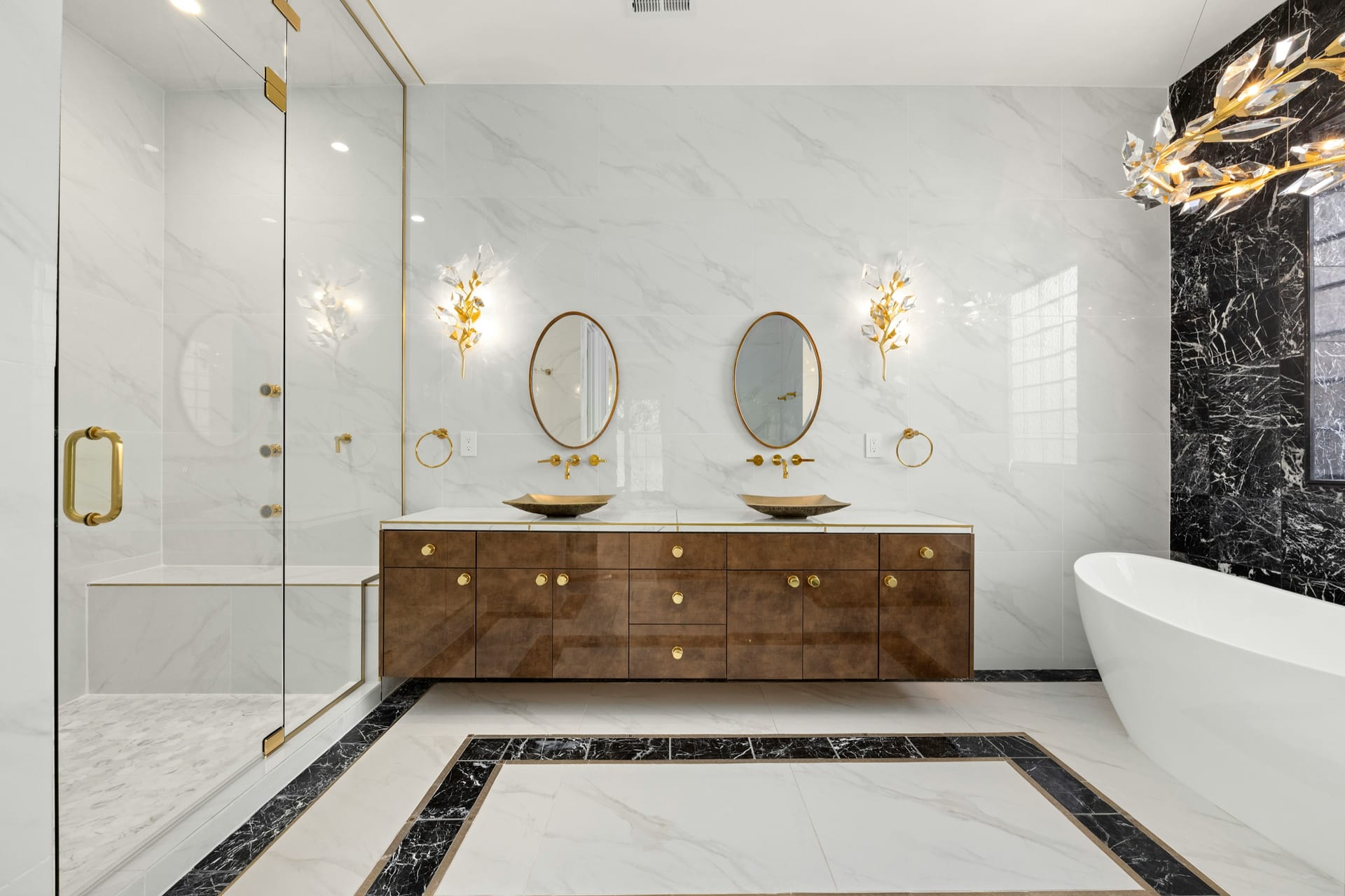 Luxury bathroom remodel with marble-look tile, brass fixtures, green vanity, and glass shower.
