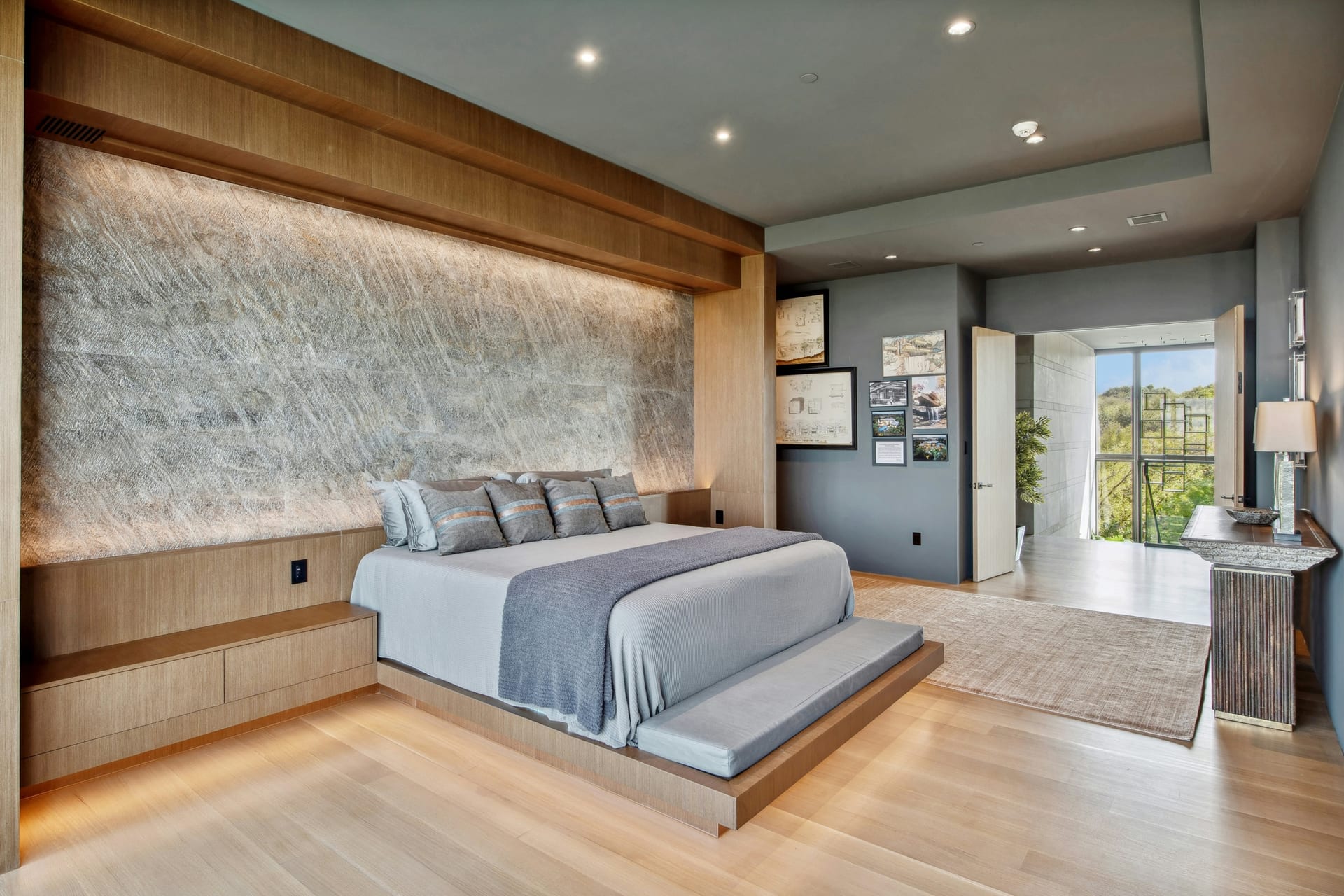 Bright open living room with custom media wall, pale wood flooring, and adjacent kitchen.